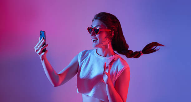 istock Amazed young woman using mobile phone isolated on neon background. digital media technology 5g concept. 1399865313