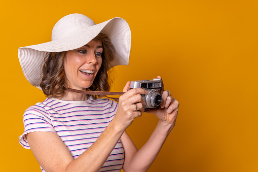 Caucasian girl in tourist concept with hat and photo camera enjoying vacation, yellow background
