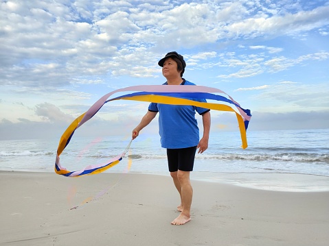 An Asian woman is learning to play gymnastic ribbon by the beach.