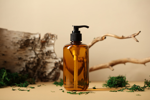 Amber glass pump dispenser bottle with natural shampoo. Tree branch, bark birch, moss on background.