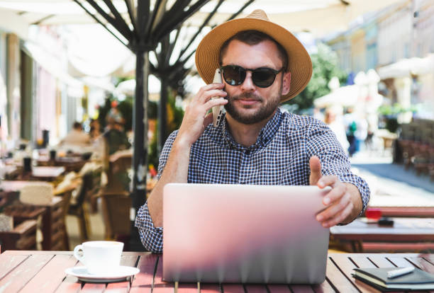 istock Casual man using laptop and calling on the mobile phone while sitting in outdoor cafe. 1399875531