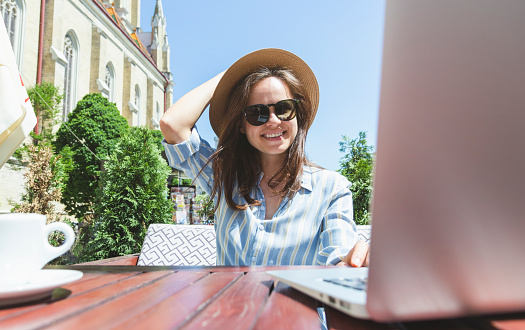 Smiling young woman sitting in sidewalk cafe and using laptop.