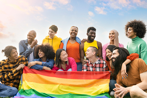 group of diverse young people having fun outdoors laughing together with gay flag protesting lgbt