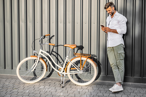 Commuter with bicycle in the city using smartphone against gray background
