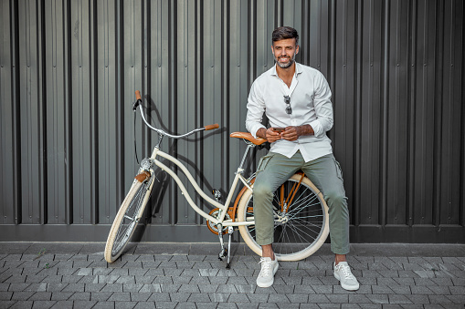 Handsome Young man with bicycle using smartphone in a city against gray background. Handsome man using smartphone. Communication, connection, business, people, mobile apps, modern lifestyle, technology concept
