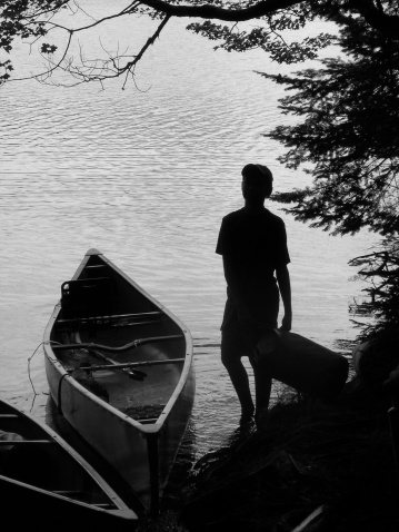 Monochrome silhouette of boy loading a canoe. Saranac Lakes,  Adirondacks, NY