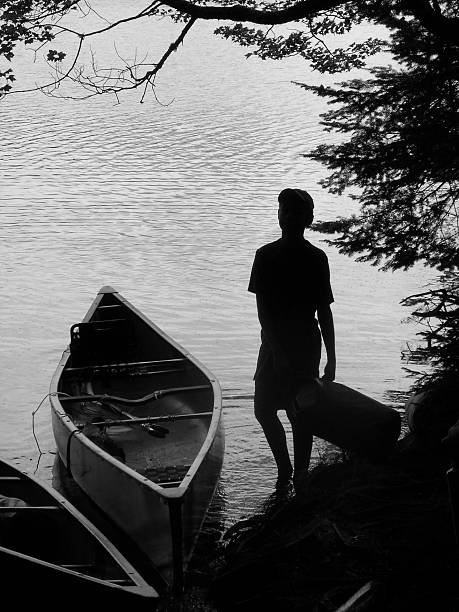 Youth Loading Canoe Silhouette Monochrome silhouette of boy loading a canoe. Saranac Lakes,  Adirondacks, NY portage valley stock pictures, royalty-free photos & images