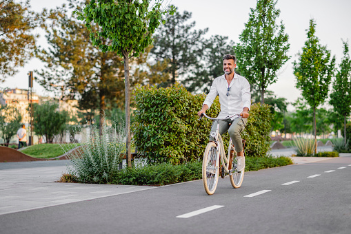 Young businessman going to work by bike. Man riding bicycle on sidewalk