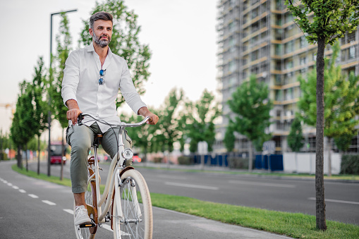 Young businessman going to work by bike. Man riding bicycle on sidewalk