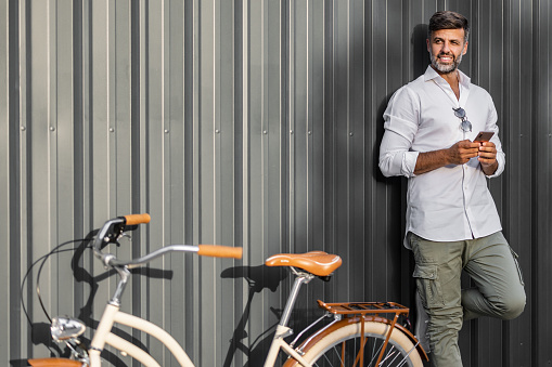 People, Communication, Technology, Leisure and Lifestyle - Hipster Man With Smartphone Against Gray Background while Standing Next to a Bicycle