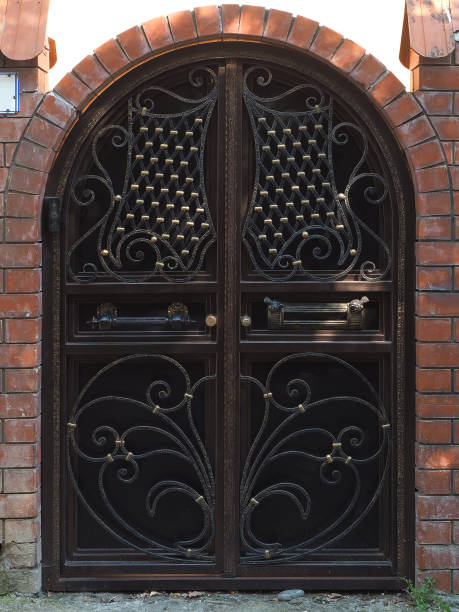 istock Iron dark gate with a gilded pattern next to a brick fence with an arch. Private area 1399887580