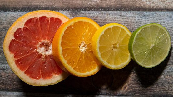 Stock photo of four citrus fruit halves in a row on a wooden chopping board, modern minimalist photo of circular sliced oranges, lemon and lime citrus fruit showing segments, seeds / pips and rind around edge, healthy eating concept photo for vitamin C and fruit juice.