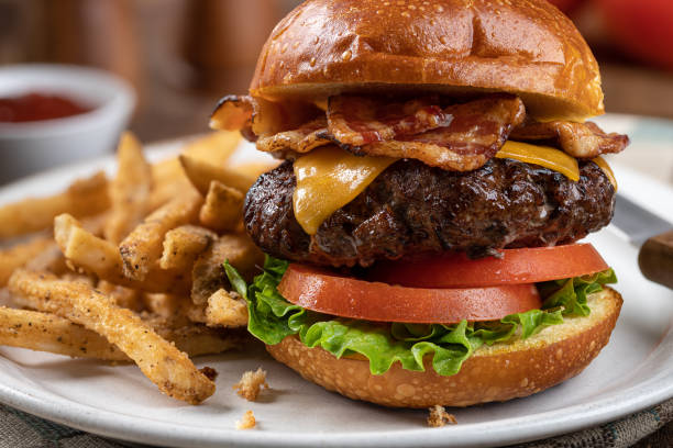 Bacon cheeseburger on a toasted bun Closeup of a bacon cheeseburger with lettuce and tomato  on a toasted bun and french fries on a plate bacon cheeseburger stock pictures, royalty-free photos & images