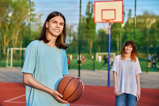 Outdoor portrait of a teenage boy with a basketball ball, on a sports ground.