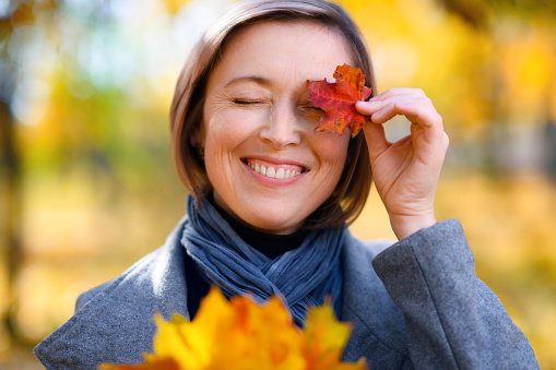 portrait of a beautiful woman with colorful yellow leaves, posing in a city park, bright sunny day in autumn