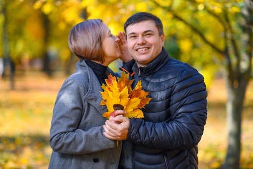 portrait of a romantic couple in an autumn city park, a man and a woman posing, they hold yellow leaves and kiss, a bright sunny day