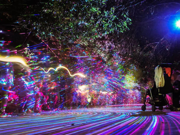 istock Bright multi-colored lines glow on the alley in the night park creating a pattern on the defocused background of people walking. Play of light and shadows. Long exposure photo 1399892448