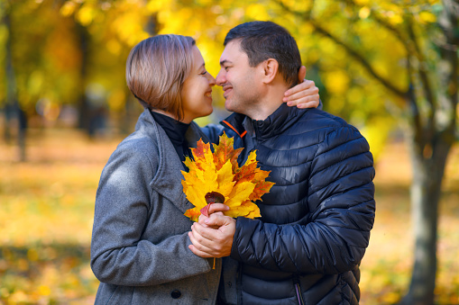 portrait of a romantic couple in autumn city park, man and woman posing with yellow leaves, bright sunny day
