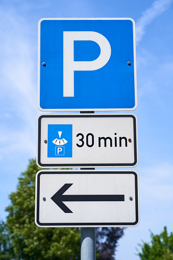 Signs with the information that cars with a parking disc can park for 30 minutes. There is a sign with an arrow pointing to the left. Three individual traffic signs.