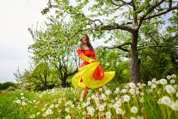 Beautiful young indian woman in long orange dress in an apple orchard