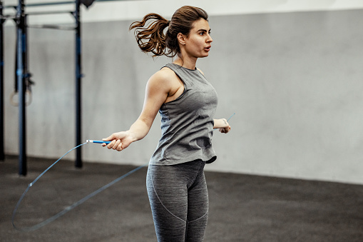 Athletic woman doing intense cardio training on jumping rope in gym