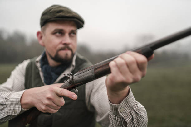 istock Hunter man in traditional shooting clothes on field aiming with shotgun. 1399905521