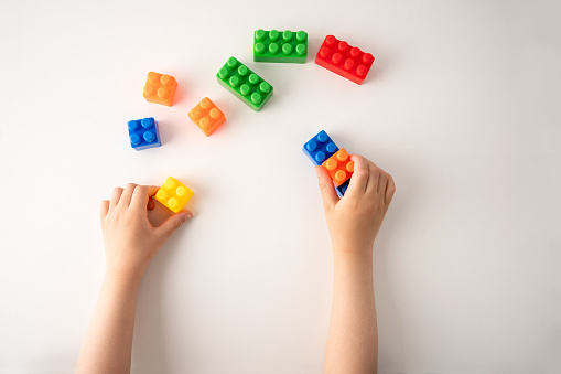 High angle shot of a child is playing with colorful construction blocks and kid hands with bricks toy on white background educational toy.