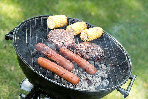 Grilling hot dogs and hamburgers with corn on the cob outside in the summer