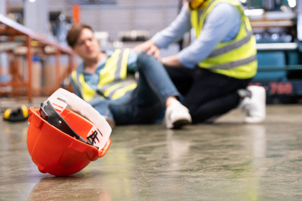 帽子に選択的に集中し、男性労働者は、彼の同僚が緊急援助と助けを与えるために来ている間、工業工場の内部で起こる事故から痛みと痛みを感じます。工場での事故。 - construction worker hardhat safety manual worker ストックフォトと画像