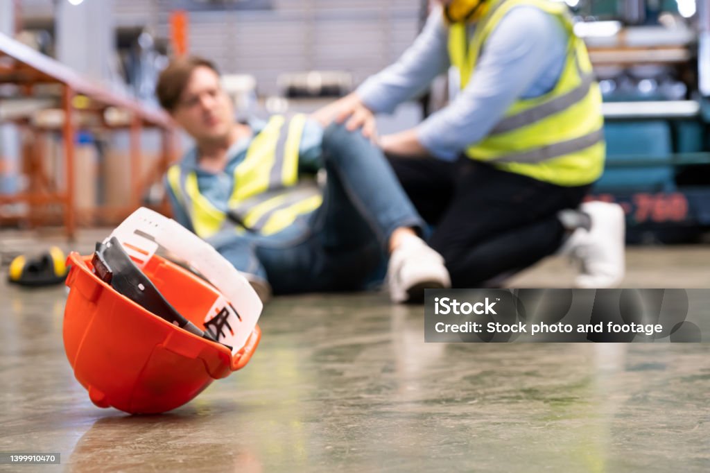 Selective focus at hat, Men worker feel painful and hurt from the accident that happen inside of industrial factory while his co-worker come to give emergency assistance and help. Accident in factory. Falling Stock Photo
