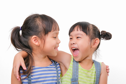 Two little sisters hugging and looking at each other isolated on white background. Two pretty little girls sisters happily cuddle and laugh. friendship and love concept.
