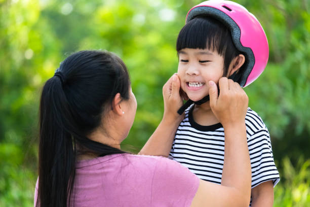 istock Asian mother helps daughter put on protective pads and safety helmet before practicing roller skating in the park. Exciting outdoor activities for kids. 1399913401