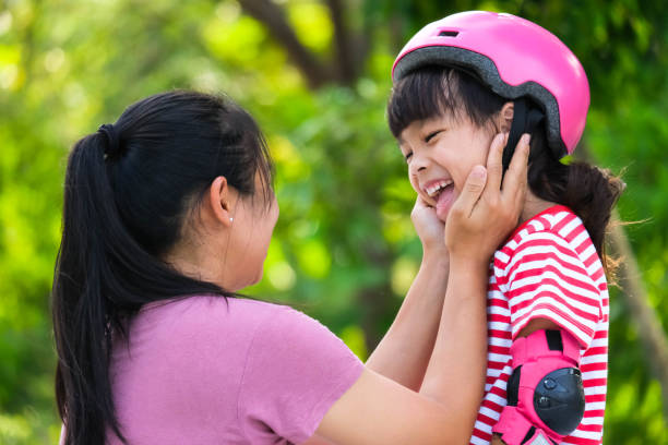 istock Asian mother helps daughter put on protective pads and safety helmet before practicing roller skating in the park. Exciting outdoor activities for kids. 1399913408