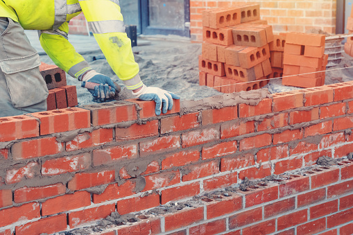 Bricklayer in safety vest and a helmet laying a brick wall using a trowel