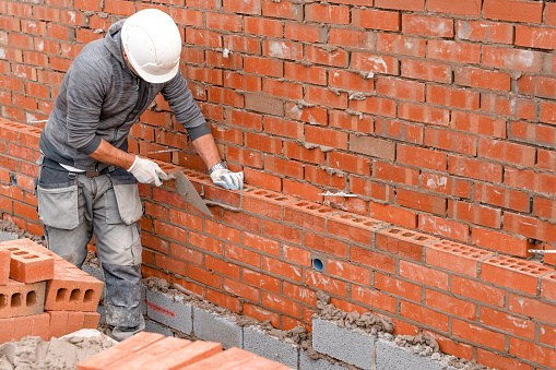 Bricklayer laying bricks on mortar on new residential house construction