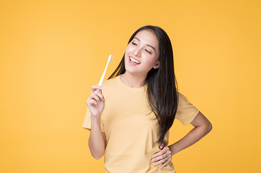 Portrait of Happy Asian female brushing her Teeth. Young Asian Woman brushing her teeth with clean white teeth. Happy Asian Woman wearing Yellow T-shirt standing over yellow background.