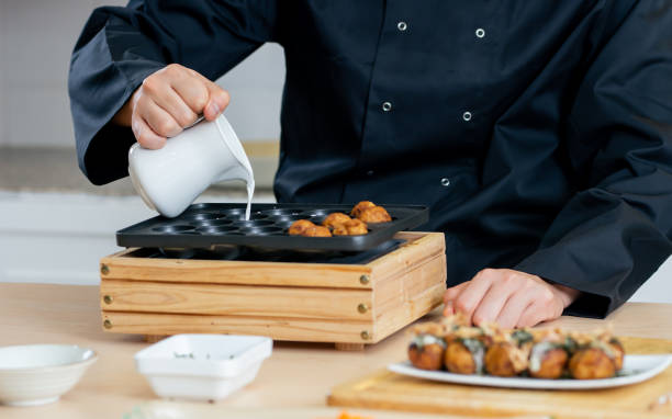 Close up and selective focus on chef hand pouring flour, milk in grill pit pan for cooking and making ball dumpling takoyaki, Japanese traditional street food. Restaurant, Hotel Concept. Close up and selective focus on chef hand pouring flour, milk in grill pit pan for cooking and making ball dumpling takoyaki, Japanese traditional street food. Restaurant, Hotel Concept cooking takoyaki is a ball shaped japanese snack stock pictures, royalty-free photos & images