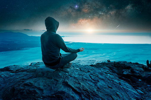 silhouette of a person in meditation position on a mountain above the night horizon
