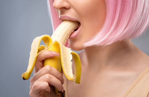 A young girl in a pink wig eats a banana.