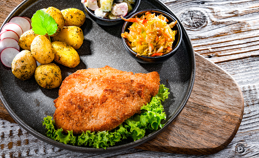 Pork breaded cutlet coated with breadcrumbs with potatoes and vegetable salads