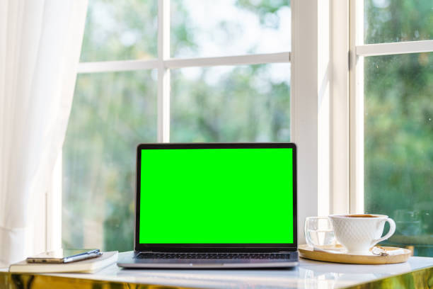 istock Mockup of laptop computer with empty screen with notebook,coffee cup and smartphone on table side the window in the coffee shop at the cafe,Green screen 1399926844