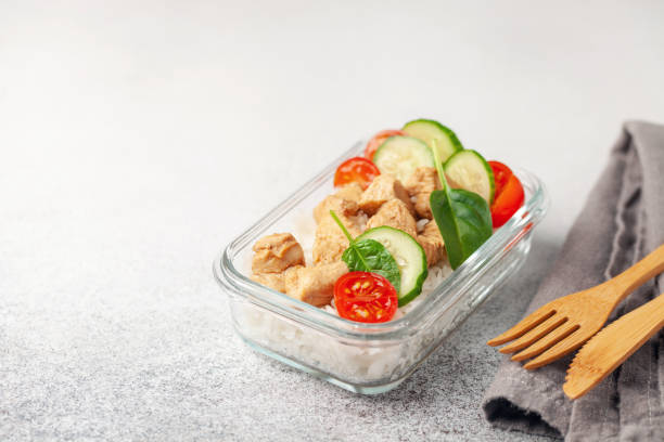テーブルの上のガラス容器に米と野菜を入れたチキンフィレ。学校、スポーツ、ビジネスフードのコンセプト - salad glass chicken garnish ストックフォトと画像