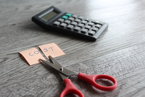 Scissor, calculator and note with text COST. Financial, cost cutting, reduce expenses concept