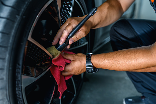 Professional car service worker polishing luxury car rim with a microfiber rag.