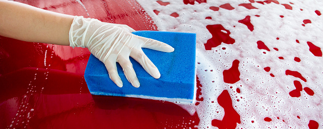 Cheerful beautiful Asian woman washing a modern red car by using a high pressurized foam and car wash sponge.