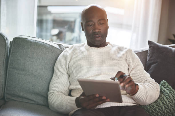 istock A man using a digital tablet while relaxing on the sofa at home. A young man browsing online with a touchscreen on the couch 1399934611