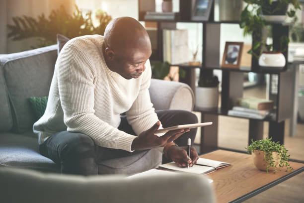 istock A man using a digital tablet and working with paperwork at home. A young man paying bills, planning his finance online with a touchscreen on the sofa 1399934945