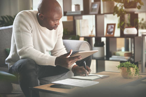 istock A man using a digital tablet and working with paperwork at home. A young man paying bills, planning his finance online with a touchscreen on the sofa 1399934946
