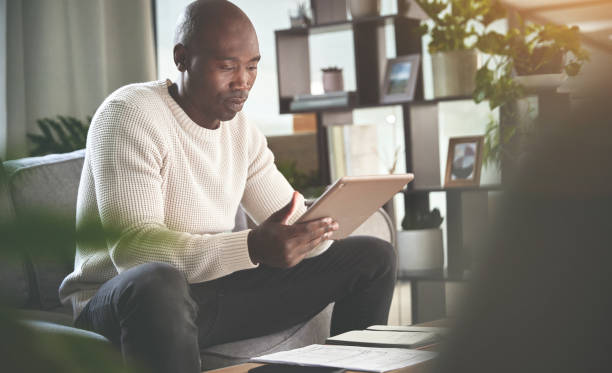 istock A man using a digital tablet and working with paperwork at home. A young man paying bills, planning his finance online with a touchscreen on the sofa 1399934948