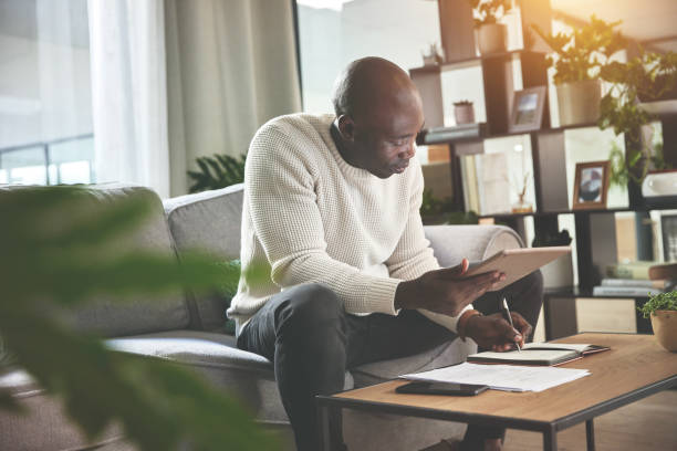 istock A man using a digital tablet and working with paperwork at home. A young man paying bills, planning his finance online with a touchscreen on the sofa 1399934949